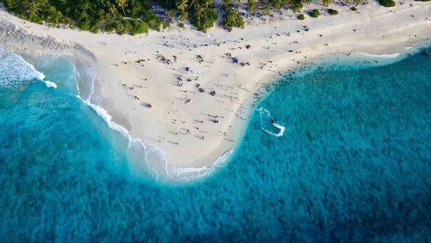 An aerial view of a beach with clear turquoise waters, sandy shore, and scattered umbrellas. - Scuba Residence (Fuvahmulah)