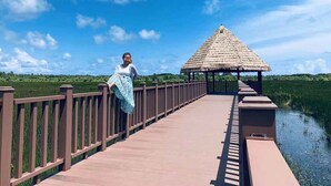 A wooden bridge with a thatched-roof structure at the end, surrounded by greenery and a clear sky. - Scuba Residence (Fuvahmulah)