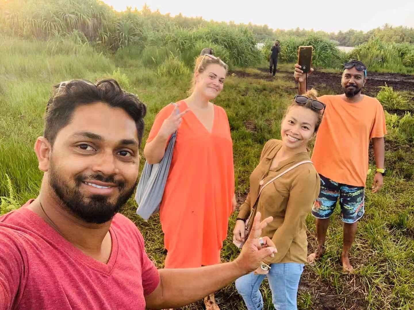 Un groupe de personnes se trouve dans un environnement naturel, avec de la végétation et une étendue d’eau en arrière-plan.