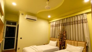 A hotel room with two beds, wooden flooring, a ceiling fan, an air conditioning unit, and a window with curtains. - Scuba Residence (Fuvahmulah)
