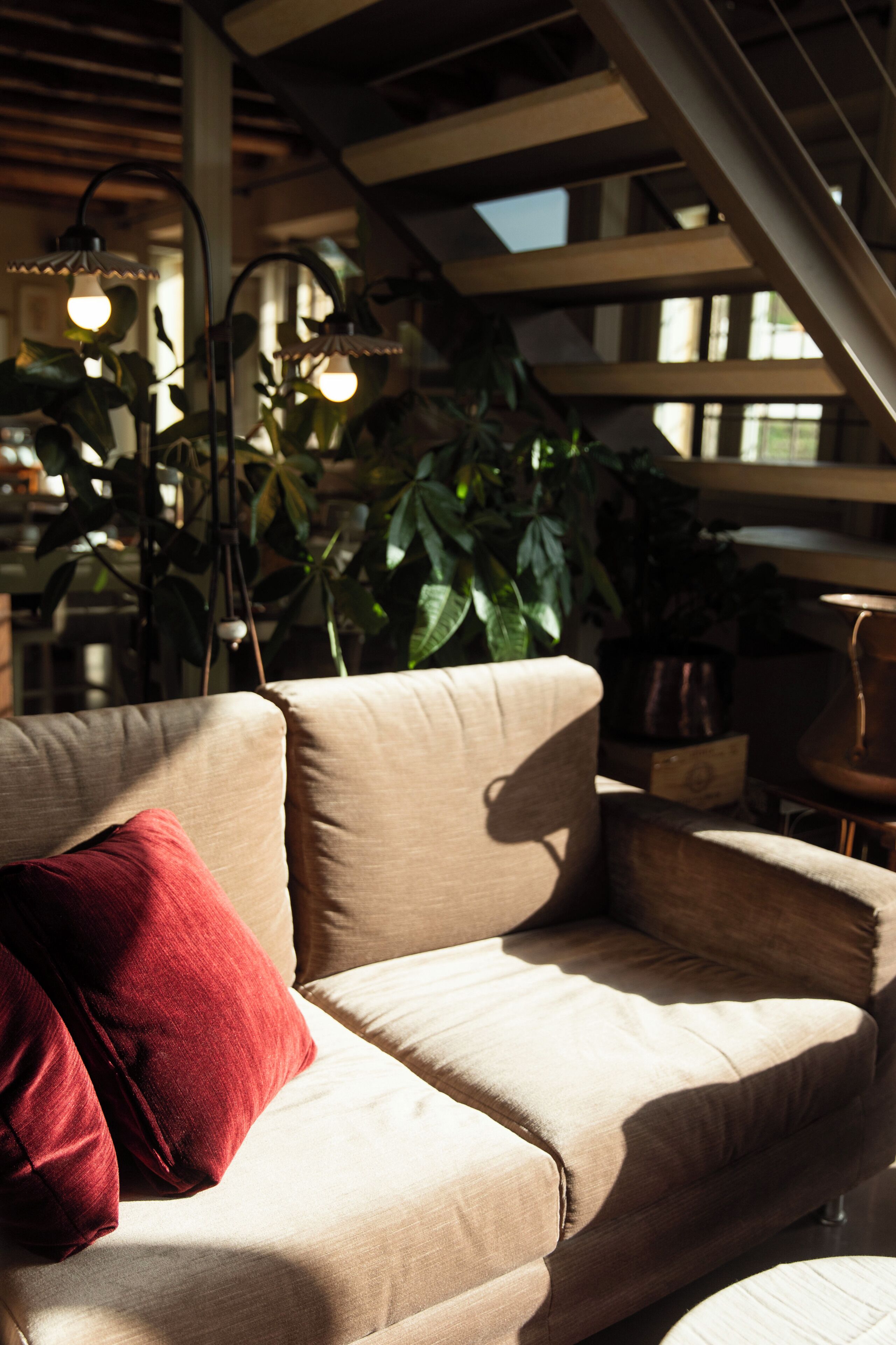 A beige sofa with a red pillow, a hanging light fixture, and a staircase in the background.