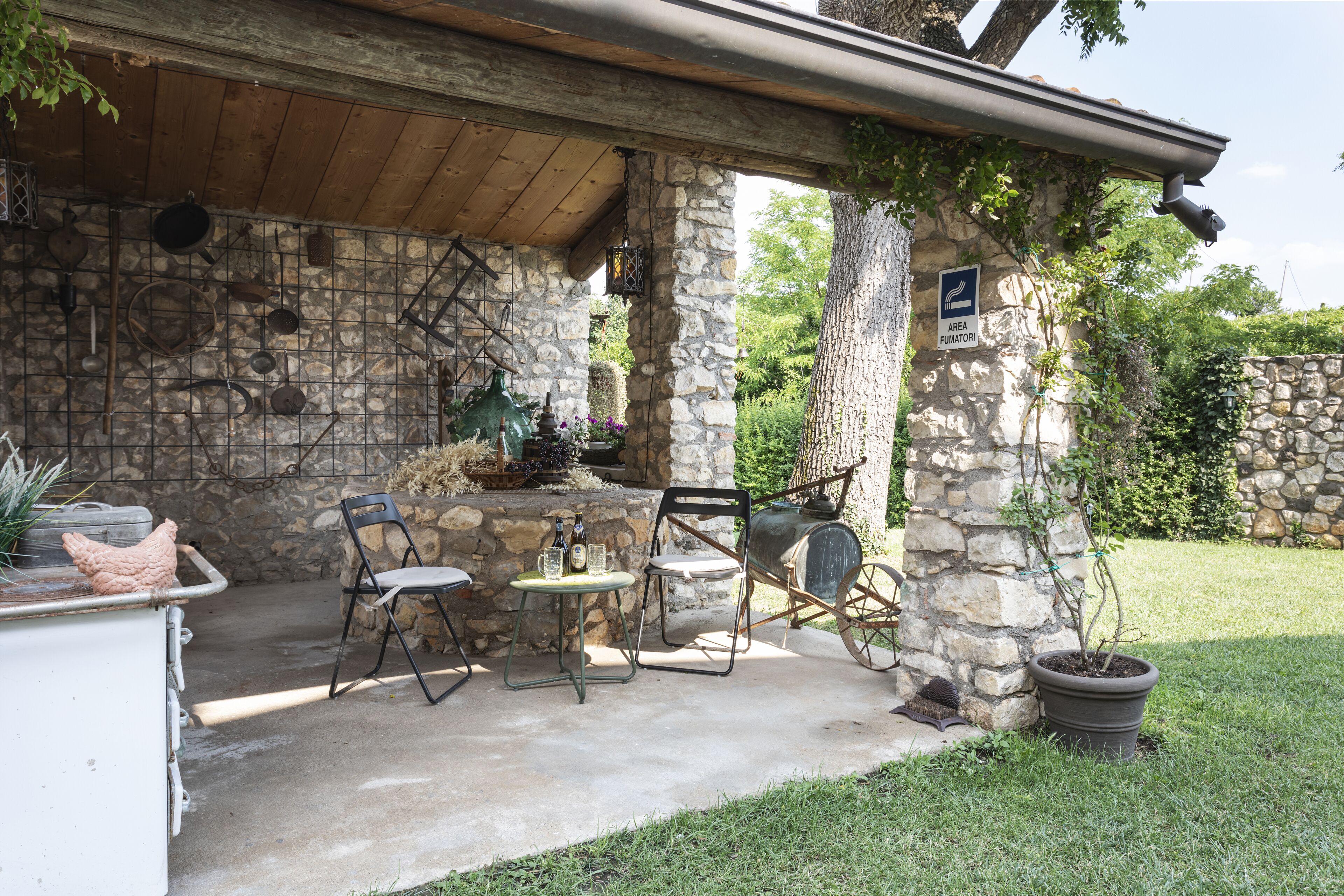 A rustic outdoor patio with stone walls, a wooden ceiling, and a stone table with chairs.