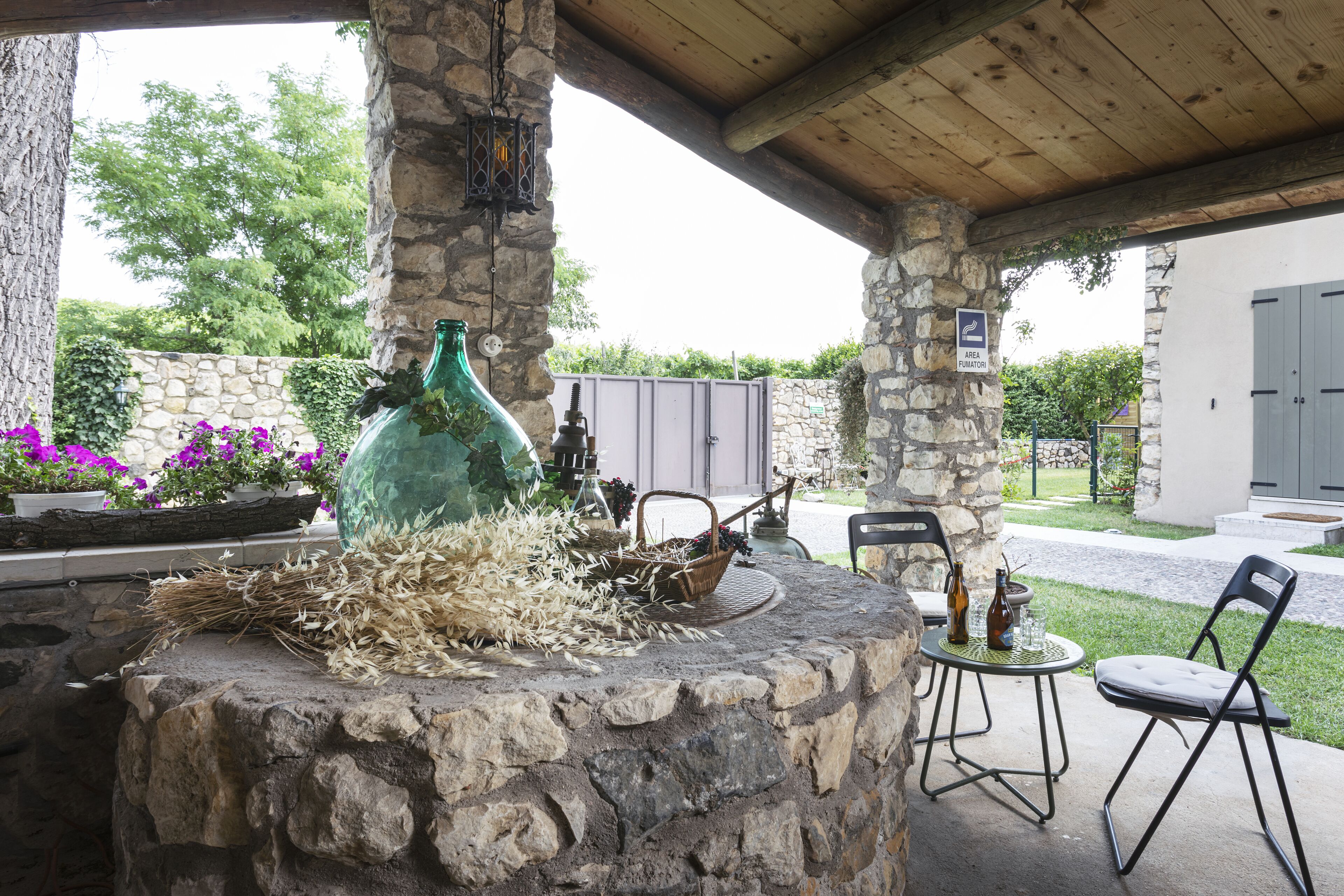 An outdoor patio with stone pillars, a rustic fire pit, and a seating area with metal chairs.