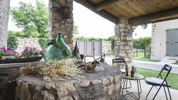An outdoor patio with stone pillars, a rustic fire pit, and a seating area with metal chairs.