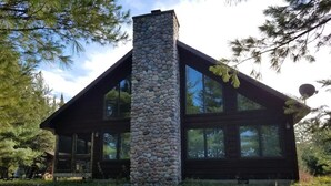 A cabin with a stone chimney, large windows, and a wooden exterior. - Piper`s Point on Lake Julia (Hiles)