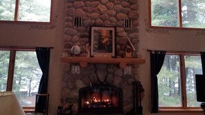 A cozy living room with a stone fireplace, large windows, and a high wooden ceiling. - Piper`s Point on Lake Julia (Hiles)