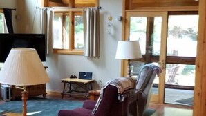 A cozy living room with wooden floors, a purple armchair, a sofa, a coffee table, a lamp, and a television. - Piper`s Point on Lake Julia (Hiles)