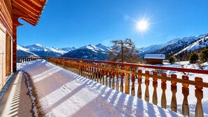 Ein hölzerner Balkon mit einem mit Schnee bedeckten Weg, der zu einer Bergblick führt.