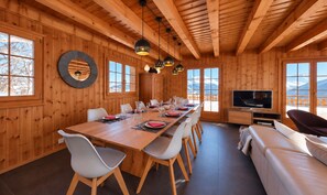 Ein Holzinterieur mit einem Esstisch für sechs Personen, einer Couch und einem Fernseher.