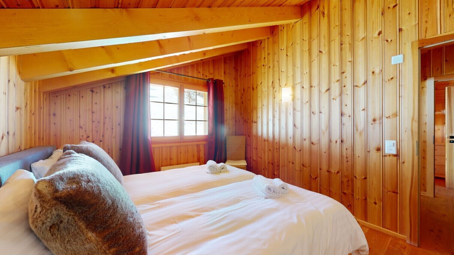 Una habitació amb panells de fusta, un llit, una finestra amb cortines i una porta.