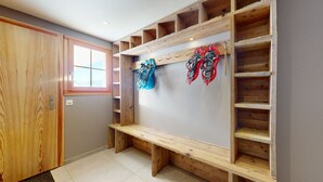 Un couloir avec un banc en bois, un porte-manteau sur lequel sont accrochées des raquettes à neige et une porte en bois.
