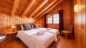Ein Zimmer in einer Holzhütte mit einem Bett, zwei Nachttischen, einem Sessel und einem Fenster mit Vorhängen.