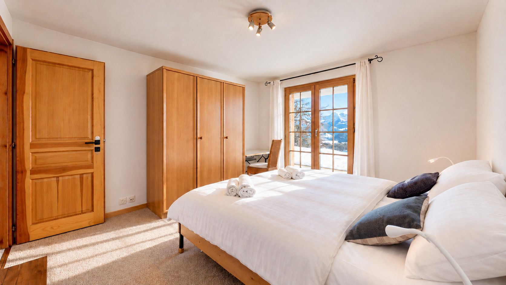 Une chambre avec un grand lit, une armoire, un bureau et une fenêtre donnant sur la montagne.