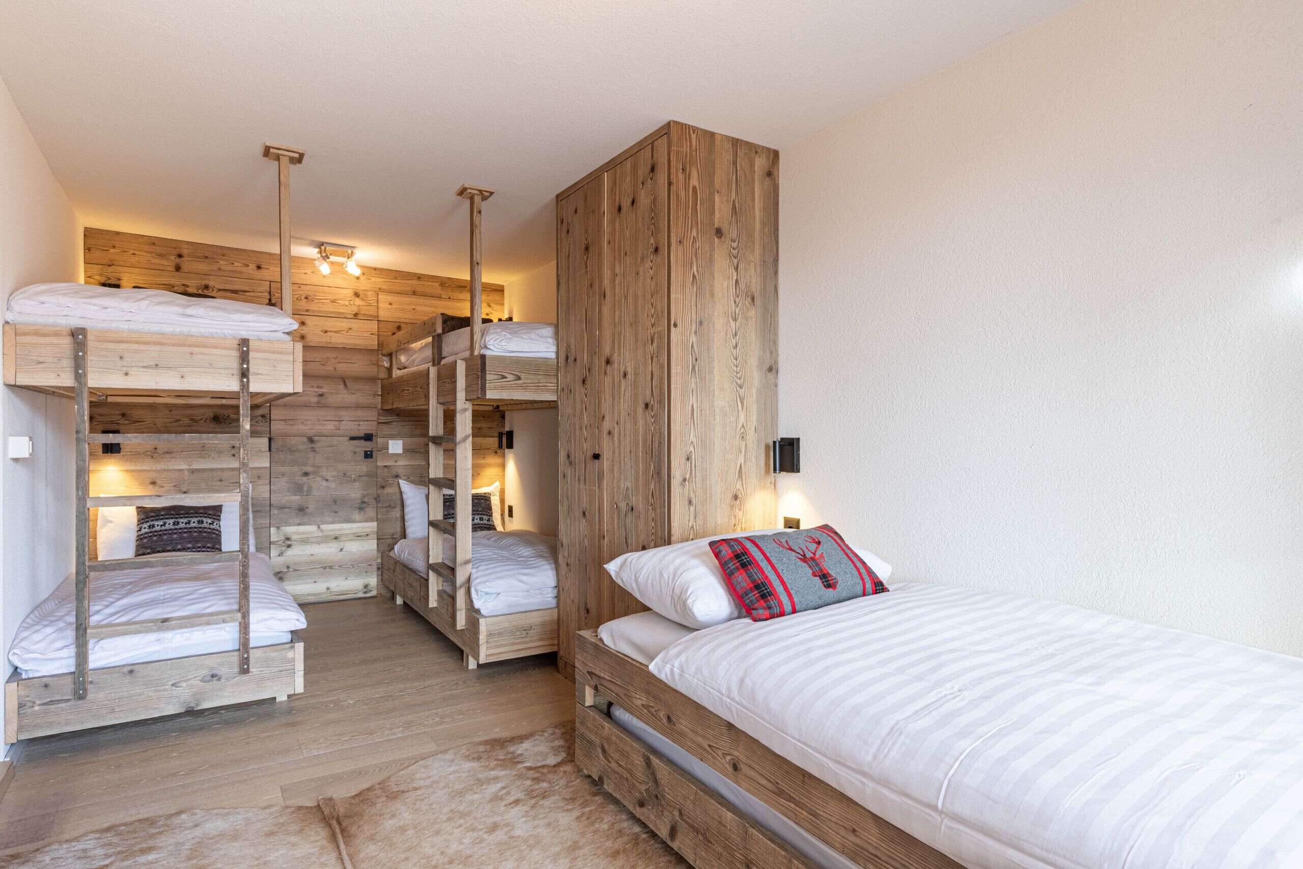 A room with bunk beds, wooden walls, and a large wardrobe.