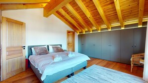 Une chambre avec un plafond en bois, un lit avec des oreillers, une armoire grise et une chaise.