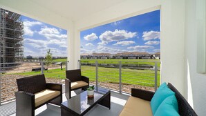 Ein Balkon mit Korbmöbeln, einem Glastisch und Blick auf eine Wohngegend mit Häusern und einem grünen Feld.