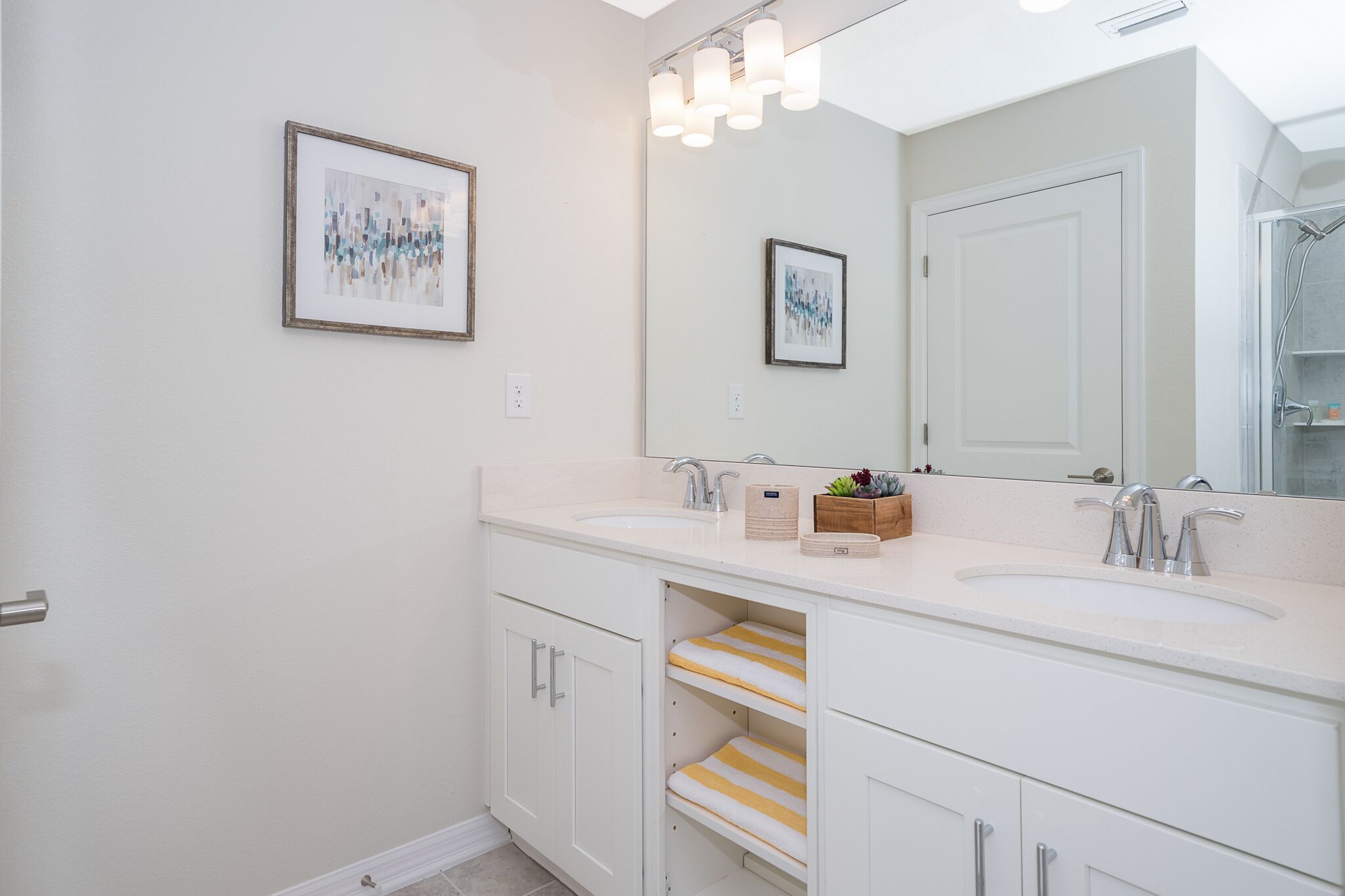 A bathroom with two sinks, a large mirror, and framed artwork on the wall.