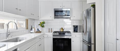 A modern kitchen with white cabinetry, stainless steel appliances, a microwave, a gas stove, and a refrigerator.