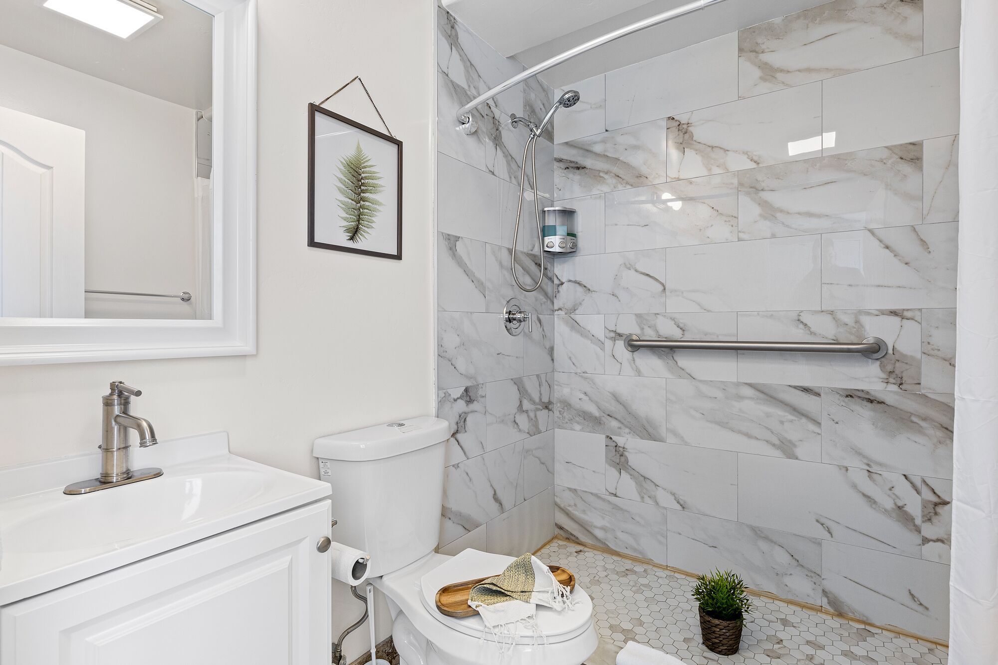 A modern bathroom with a marble shower wall, a framed plant, and a white toilet.