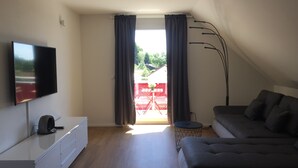 Una sala de estar moderna con un televisor de pantalla plana, un sofá, una mesa de centro y un ventanal con cortinas.