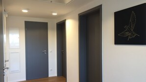 Un pasillo con suelo de madera, una puerta blanca, una puerta gris oscuro y una obra de arte ennegrecida con un pájaro.
