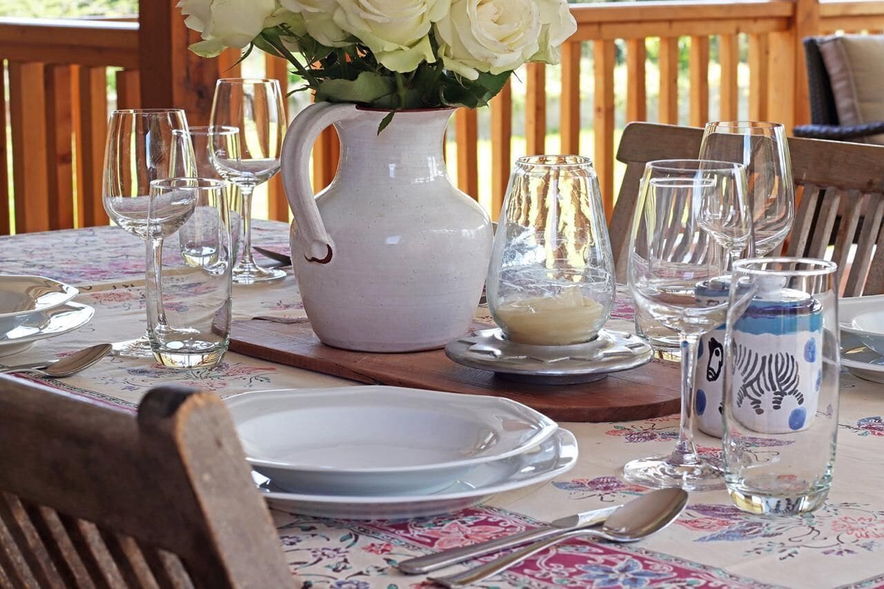 A table set for dining with white plates, clear wine glasses, a pitcher, and decorative salt and pepper shakers.