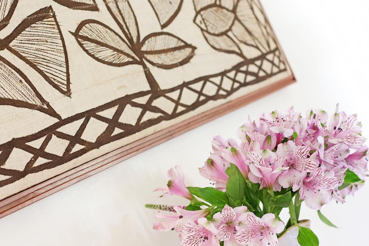 Ein gerahmtes Kunstwerk mit geometrischen Mustern und einem Strauß rosa Blumen.