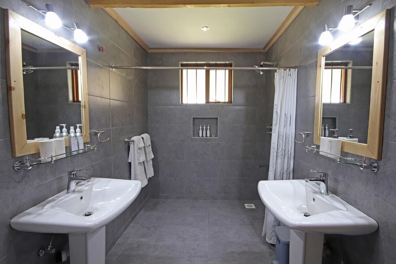 A modern bathroom with two sinks, large mirrors, and a shower area.