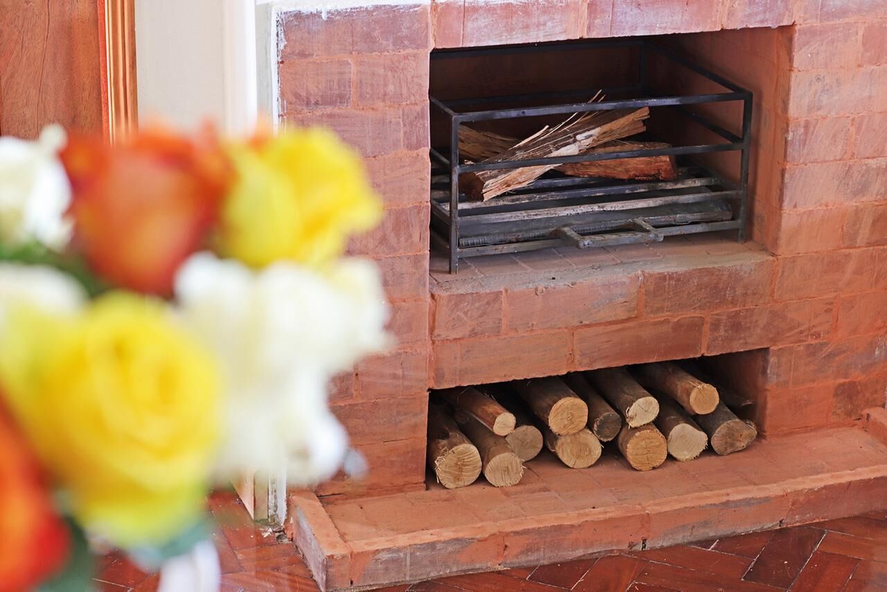 A brick fireplace with a metal shelf holding logs and a lower shelf with neatly stacked firewood.