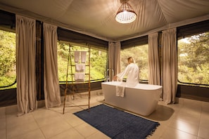 A modern bathroom with a large bathtub, a wooden ladder, and a blue rug. - Olesamara Collection (Nanyuki)