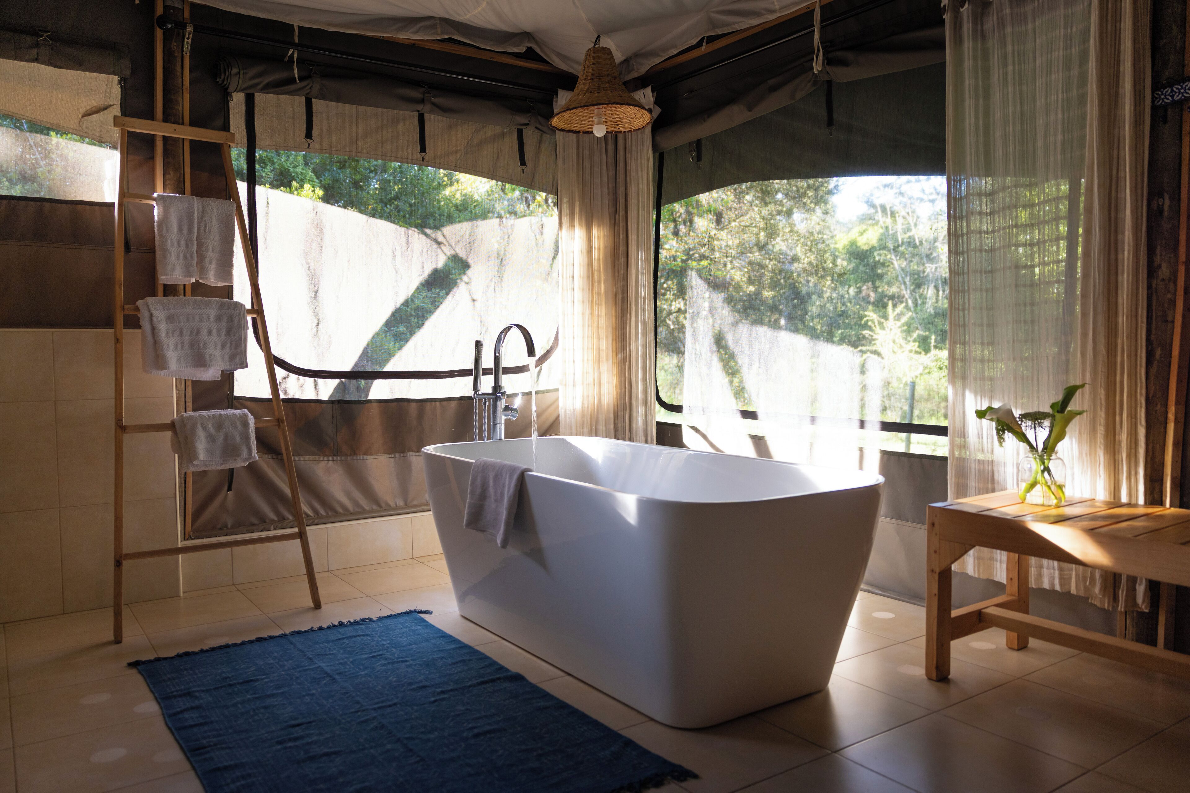 Une salle de bain moderne avec une baignoire sur pieds, une échelle en bois sur laquelle sont posées des serviettes, et une vue sur la verdure à l’extérieur.