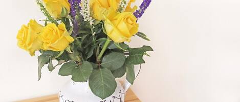 Um vaso branco com arranjo floral de rosas amarelas e flores roxas.