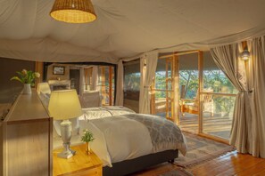 Une chambre spacieuse avec un grand lit, un bureau et une chaise. De grandes portes coulissantes offrent une vue sur l’extérieur.