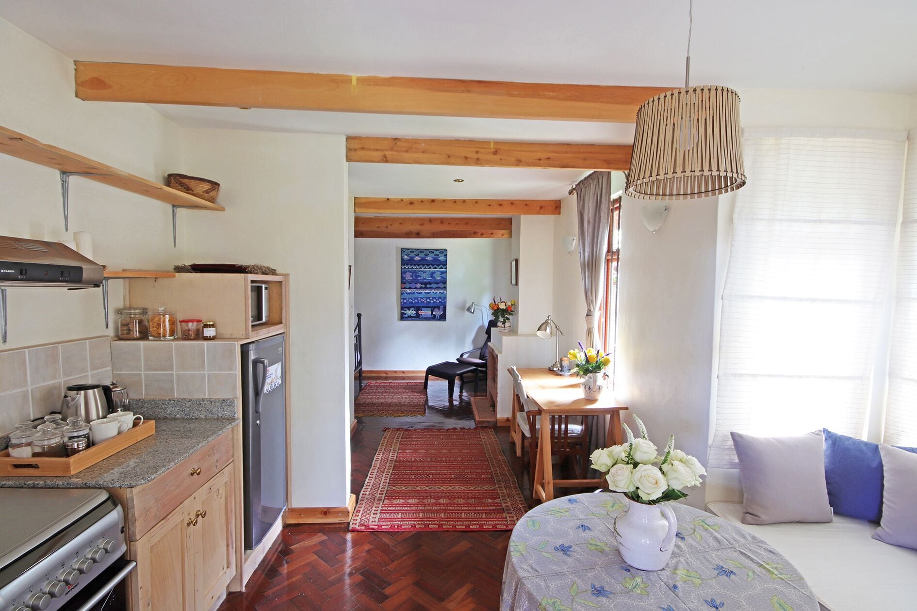 A kitchen with a stove, refrigerator, and wooden cabinets. There is a dining area with a table and chairs, and a window with curtains.