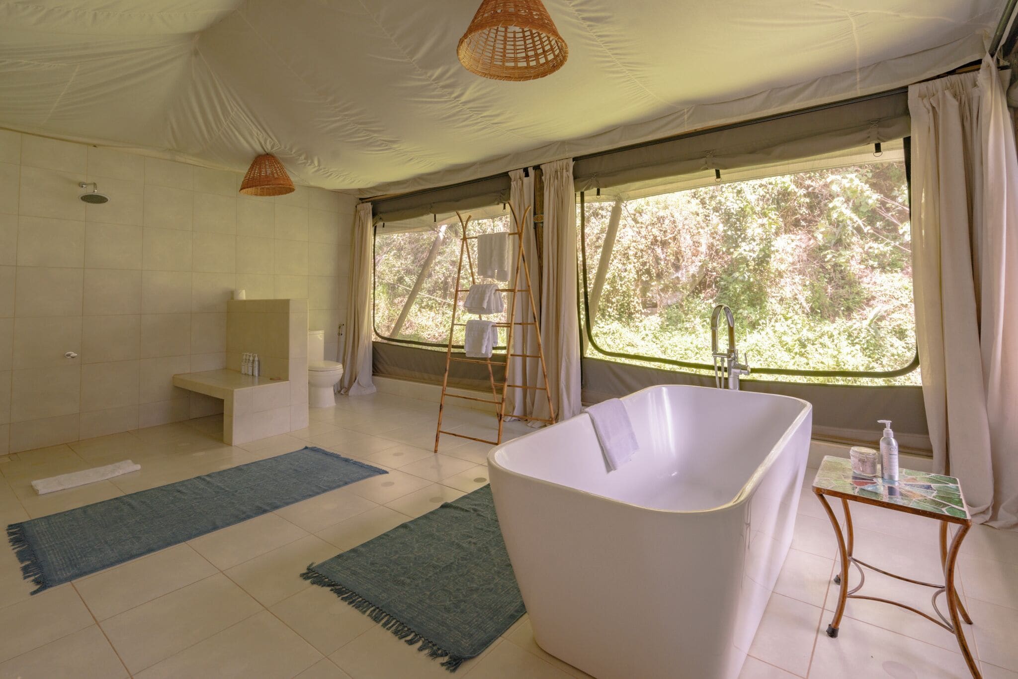 A spacious bathroom with a large bathtub, a shower, and a sink. There are two windows providing natural light and a view of trees.