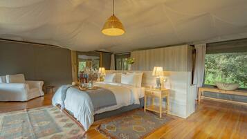 A spacious bedroom with a large bed, bedside tables, a hanging light fixture, and a view of greenery outside.