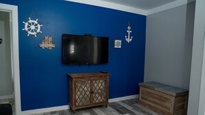 Quarto com parede azul, um armário de madeira, televisão e decoração náutica.