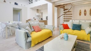 Un vaste espace de vie comprenant une table à manger, deux canapés agrémentés de coussins colorés, une table basse et un escalier menant à un niveau supérieur.