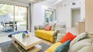 Un salon spacieux avec un grand canapé, une table basse et un coin repas comprenant une table et des chaises. Une porte-fenêtre coulissante donne accès à un patio extérieur.