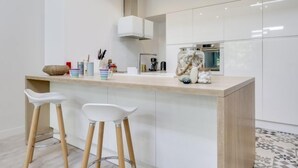 Une cuisine moderne avec des armoires blanches, un comptoir en bois et deux tabourets de bar blancs.