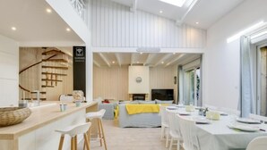 Une cuisine moderne dotée d’un îlot central, d’un coin repas avec des chaises blanches et d’un escalier menant à un niveau supérieur.