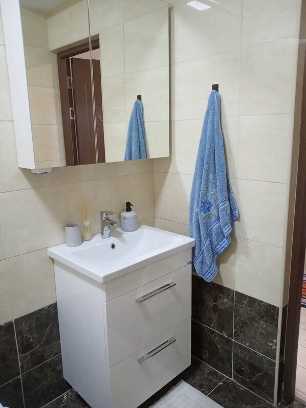 Une salle de bain avec un meuble-lavabo blanc, un miroir, un évier et un porte-serviettes.