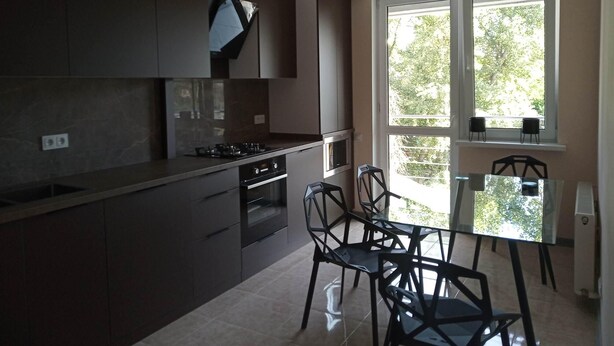 A modern kitchen with dark cabinets, a gas stove, and a dining area with a table and chairs. - Comfy & brand new downtown apartment (Chisinau)