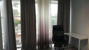 A room with a desk and a chair, large windows with curtains, and a view of greenery outside. - Comfy & brand new downtown apartment (Chisinau)