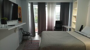 A hotel room with a bed, a desk, a chair, a TV, and a window with curtains. - Comfy & brand new downtown apartment (Chisinau)