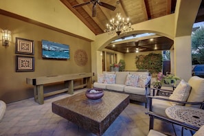A cozy living area with a stone coffee table, a sofa with patterned cushions, a bench, and a television mounted on the wall.