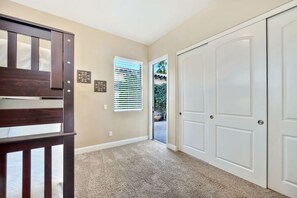 A hallway with carpeted flooring, a wooden bench, a door, and a window with blinds. - Tuscany: Pool, Spa, Fire Pit, Ping Pong Games (Indio)