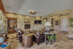 A spacious living room with a stone wall, leather furniture, a fireplace, and a ceiling fan.