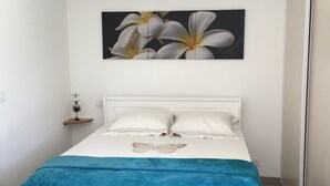 A bedroom with a bed, a blue blanket, a white headboard, a wall-mounted picture of flowers, and a hanging light fixture. - THE QUIET HOUSE BETWEEN SEA AND MOUNTAIN (MARCORIGNAN)