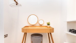 Een compacte, moderne badkamer met een houten wastafelmeubel, een ronde spiegel, een klein krukje en een potplant.